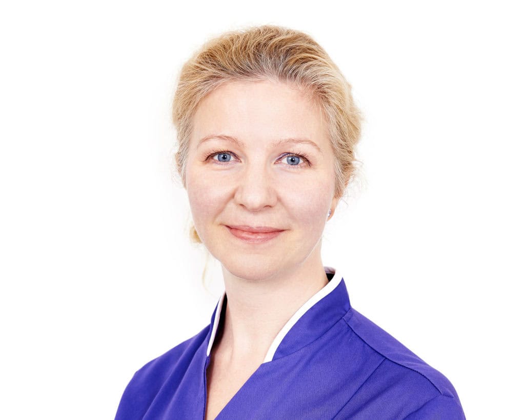 Female healthcare professional in blue uniform smiling at the camera.
